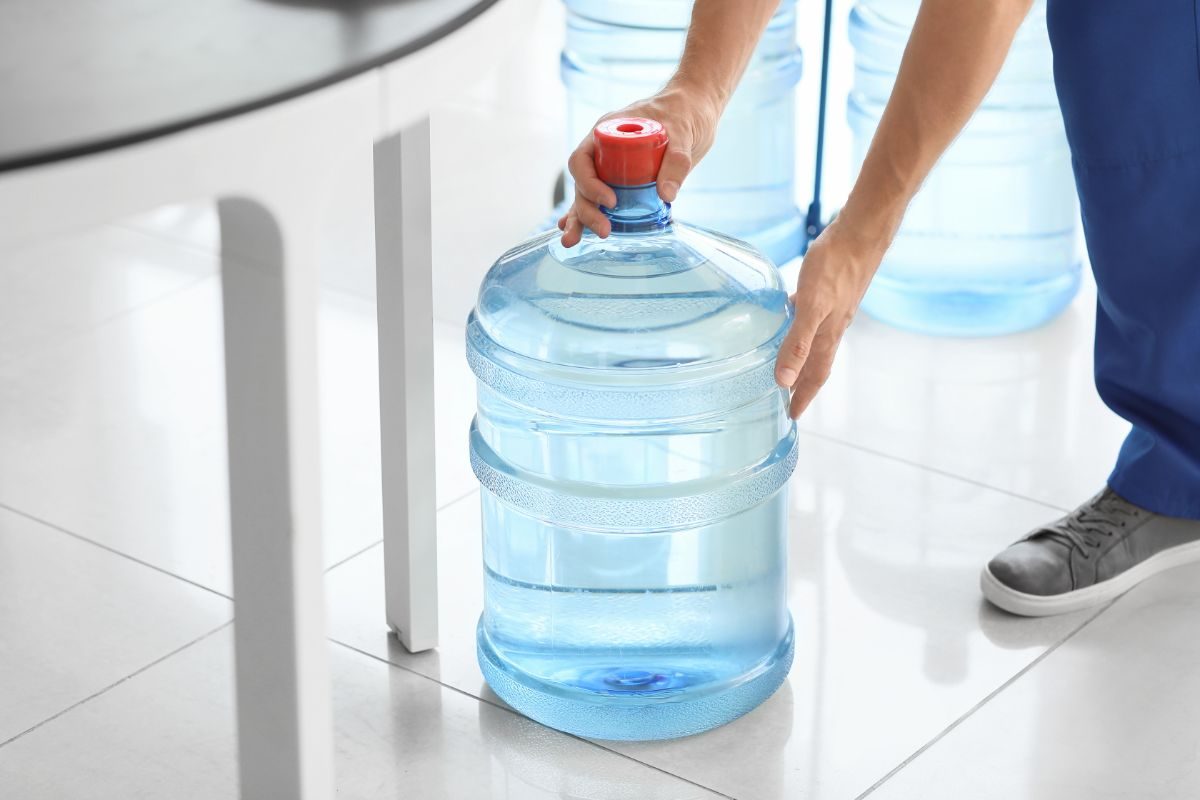 uomo che posa sul pavimento un gallone di acqua
