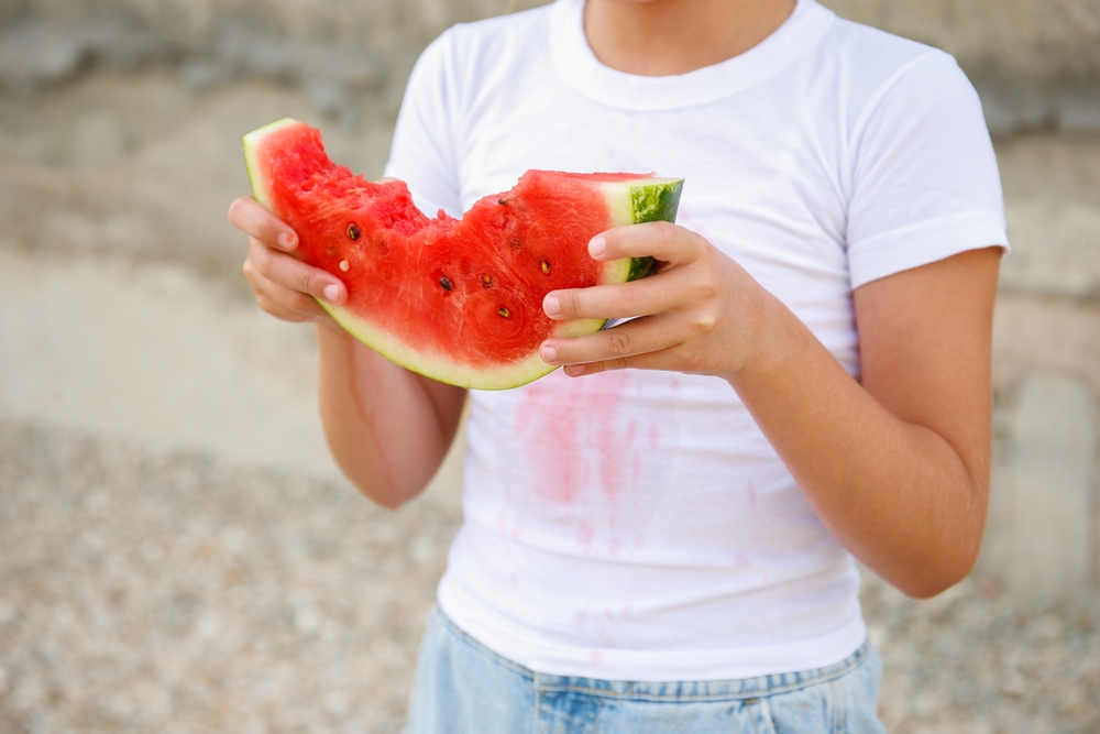 Bambino con fette di melone e macchie in camicia bianca
