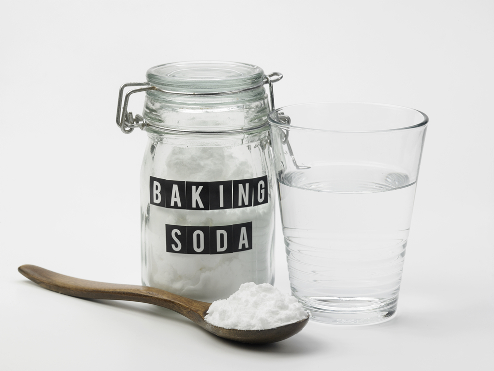 Bicarbonato di sodio in mosche Rimozione: un barattolo di bicarbonato di sodio e un barattolo di acqua limpida su una superficie bianca con piccolo bicarbonato.